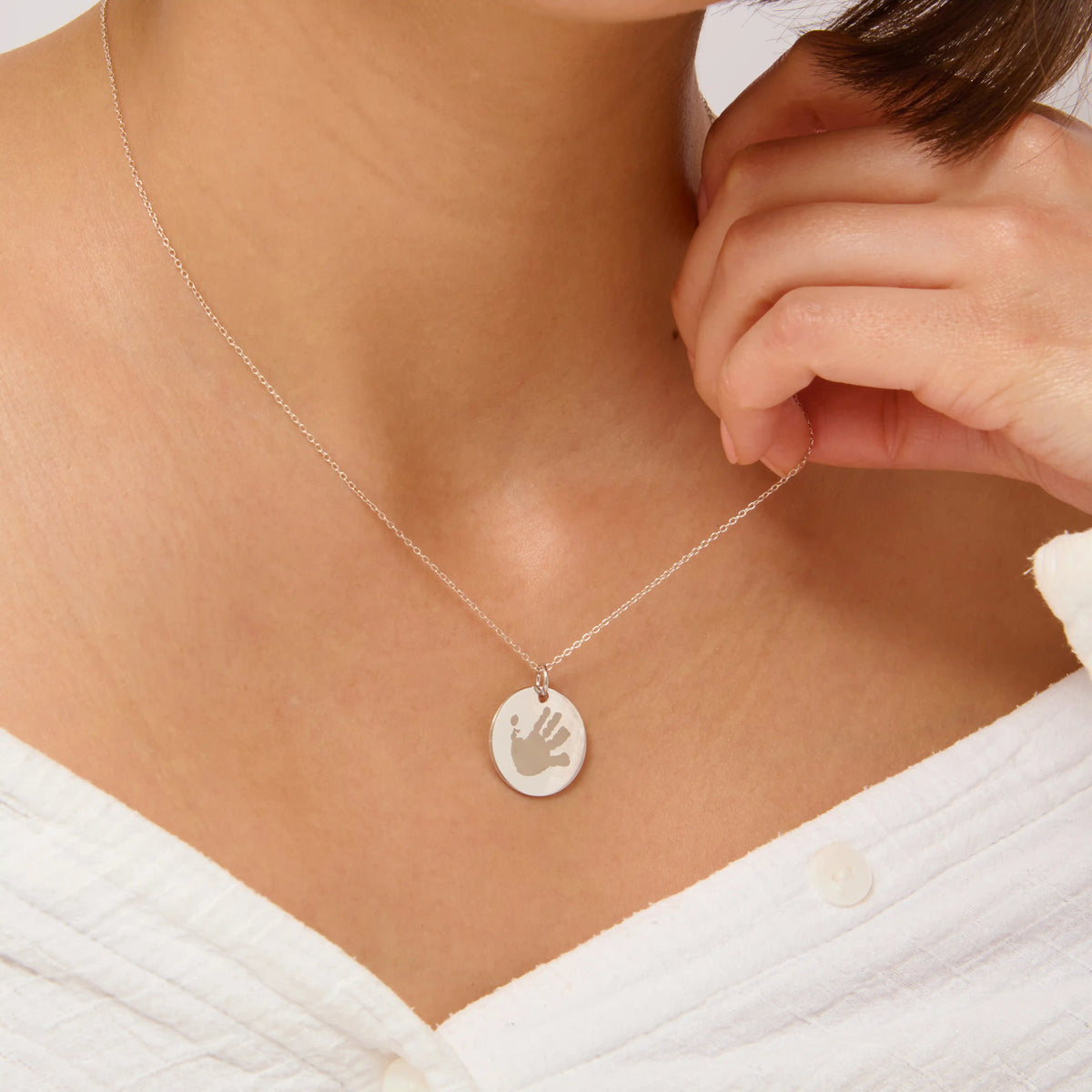 Woman holding the chain of a silver handprint pendant necklace