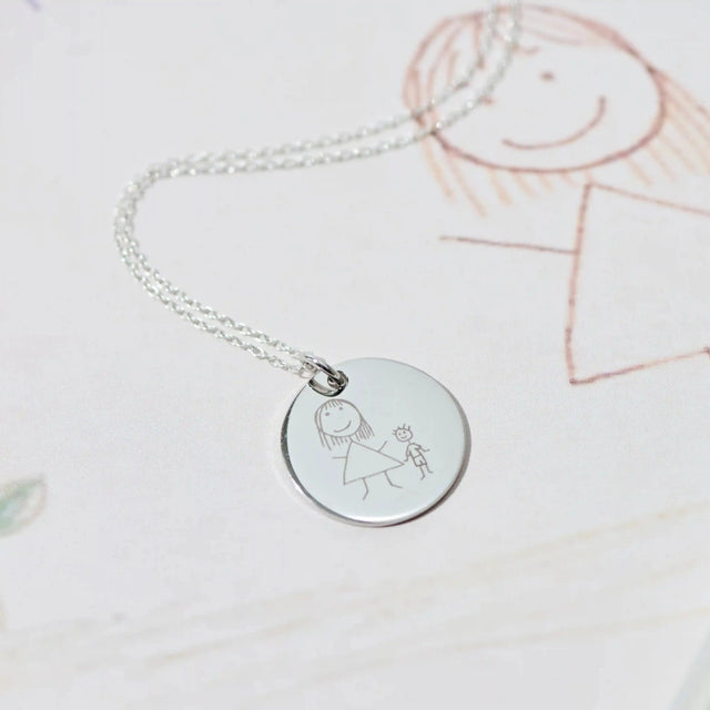 Silver pendant engraved with a child's drawing, resting on the original crayon picture