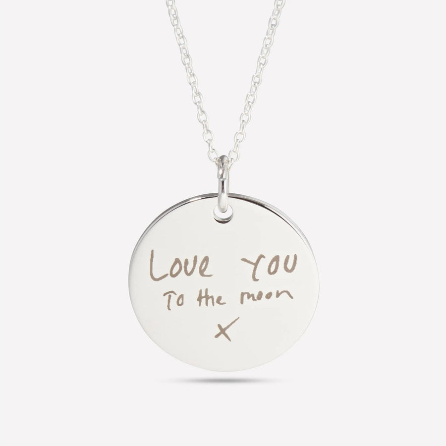 Silver pendant engraved with handwriting that reads Love you to the moon