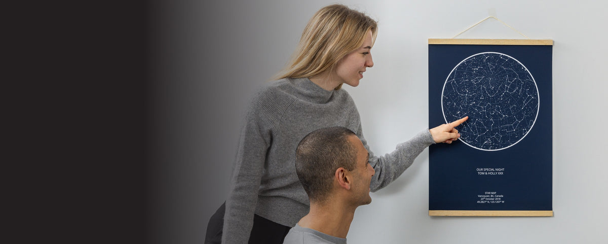 Couple hanging a personalised star map with a wooden hanger on a wall