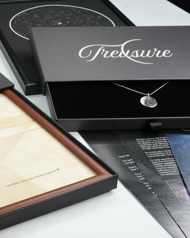 Their star, worn close to the heart: engraved silver star map pendant in its open Treasure gift box beside a framed Binary Star Name Deed, star map and Sky Atlas leaflets