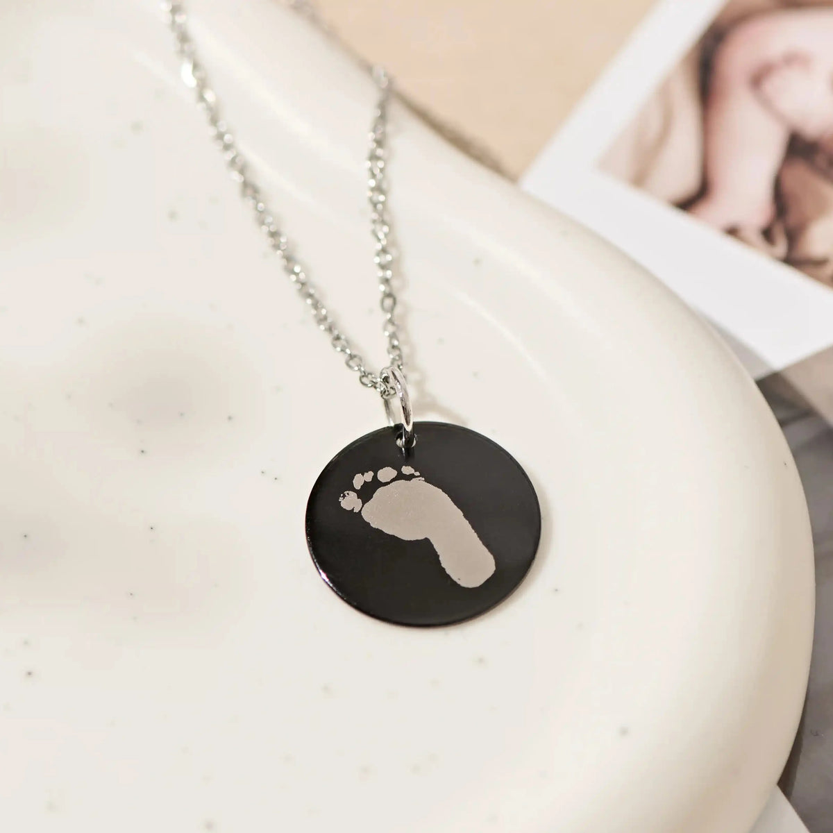 Black baby footprint pendant necklace resting on a ceramic dish
