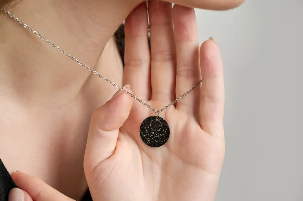 Hands holding a Starniri black star necklace with a star chart engraved on the round pendant