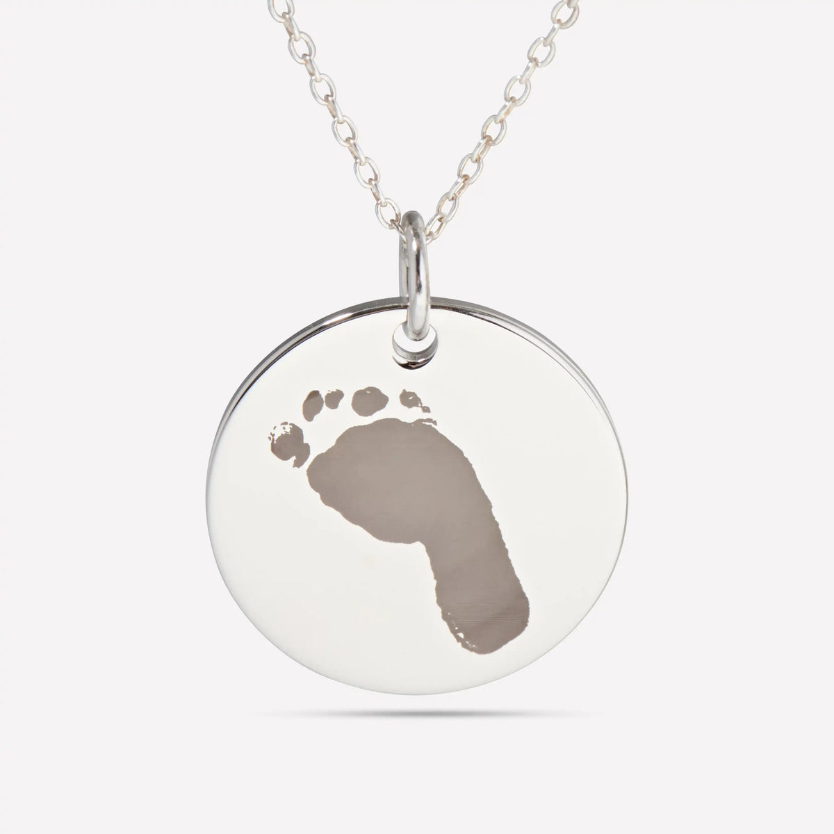 Close-up of a silver pendant engraved with a baby footprint