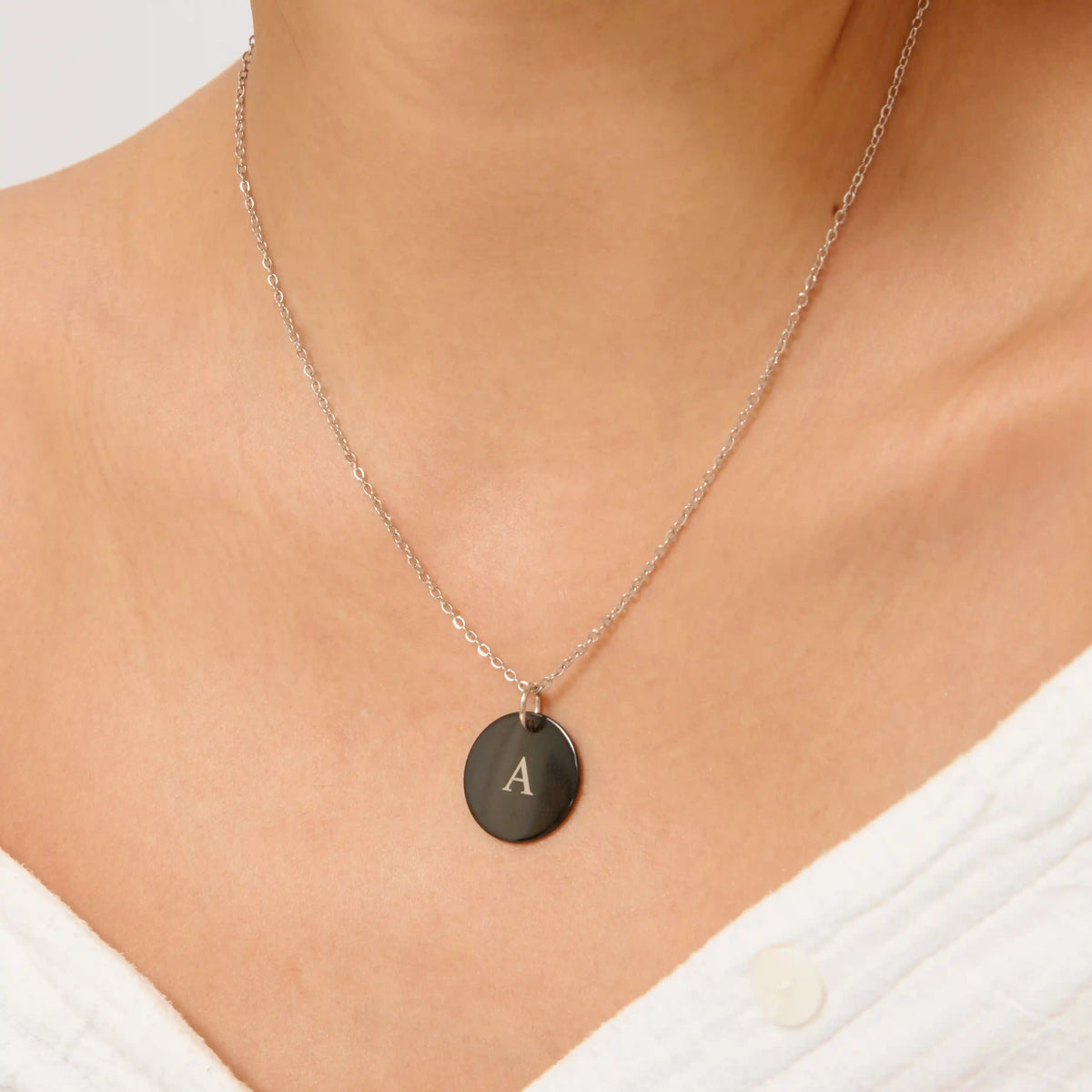 Black disc pendant necklace engraved with the initial A, worn