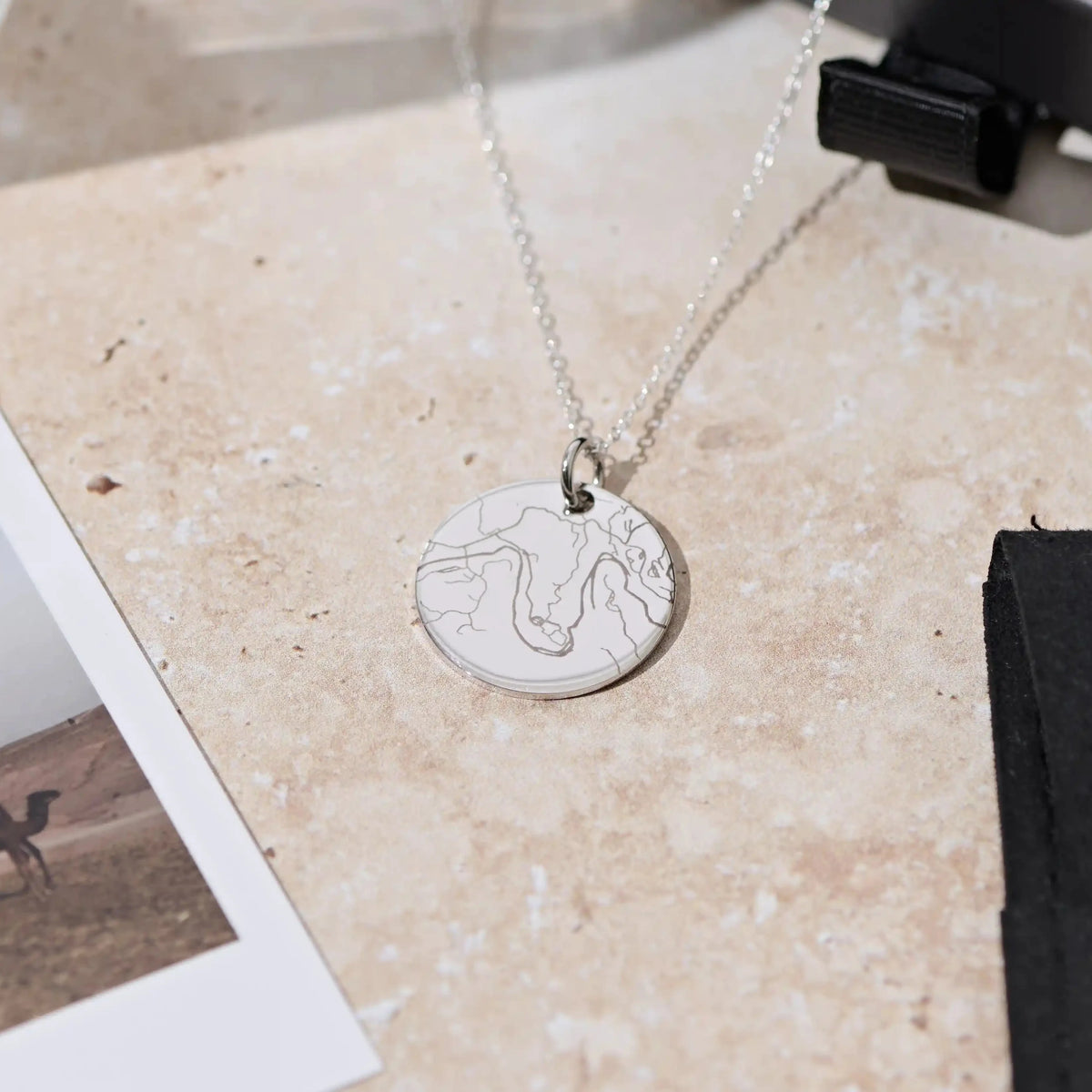 Silver street map necklace laid on a marble surface beside a photo print