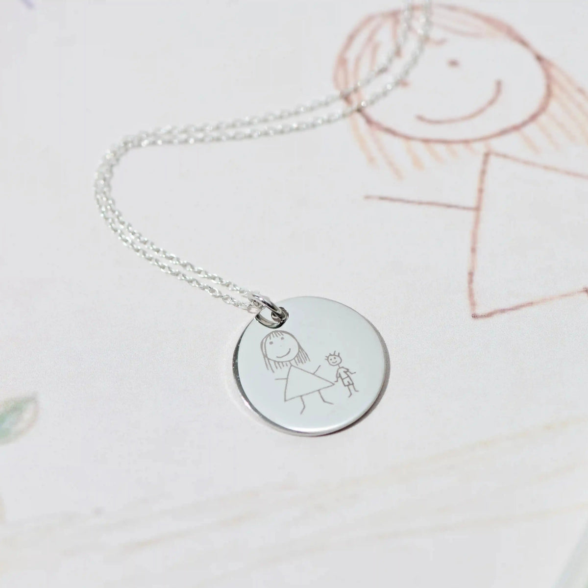 Silver pendant engraved with a child's drawing, resting on the original crayon picture