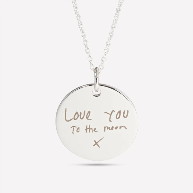 Close-up of a silver pendant engraved with the handwritten words Love you to the moon