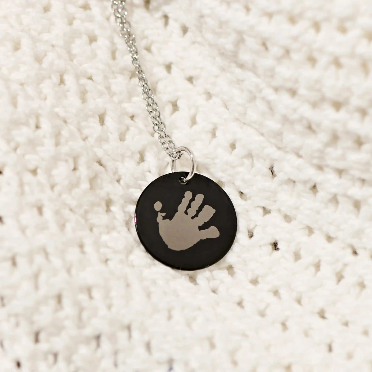 Black handprint pendant necklace on a knitted jumper