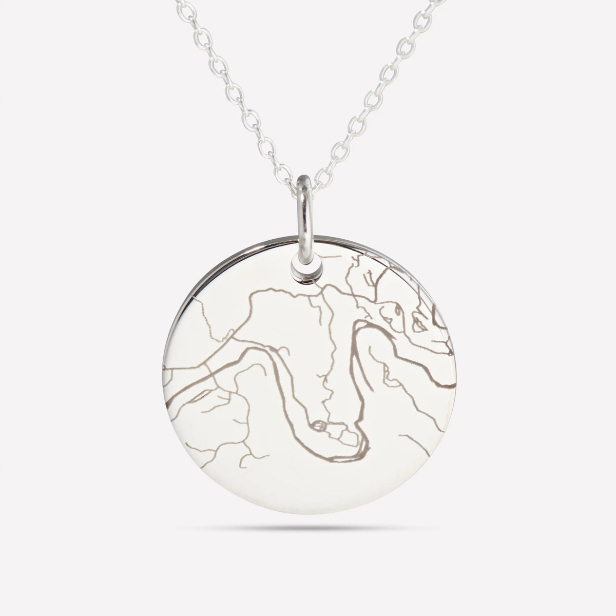 Close-up of a silver disc pendant engraved with a detailed street map