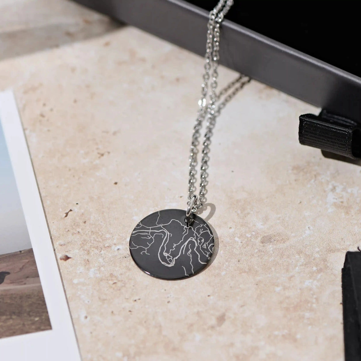 Black street map pendant on a silver chain laid on a marble surface