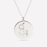 Close-up of a silver pendant engraved with a child's drawing of a family