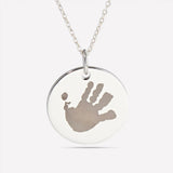 Close-up of a silver pendant engraved with a child's handprint