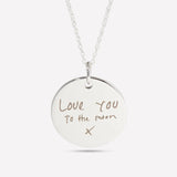 Close-up of a silver pendant engraved with handwritten "Love you to the moon"