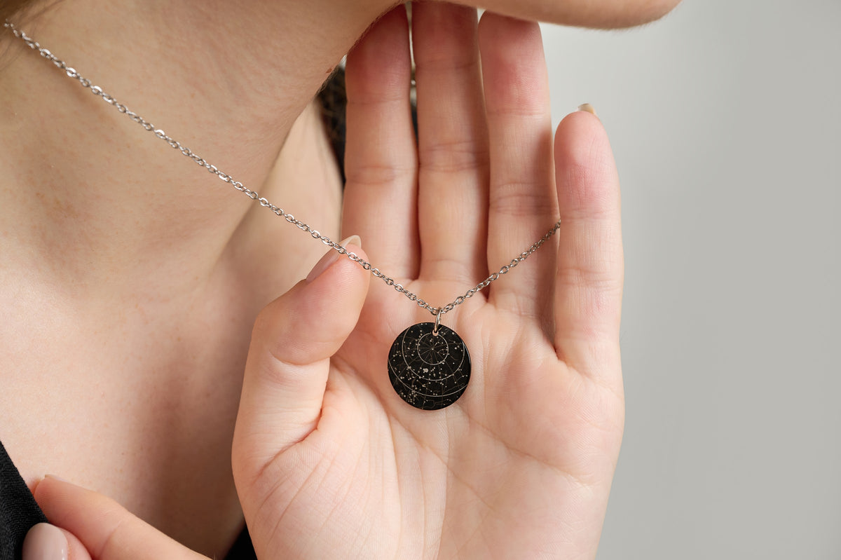 Black star map pendant necklace resting in an open palm