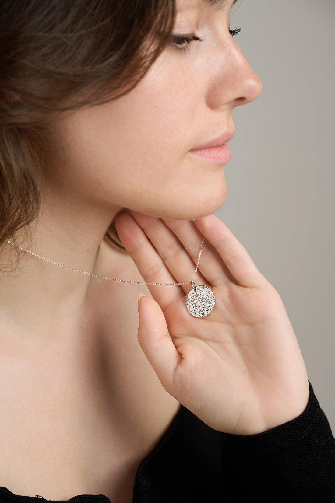 Woman holding an engraved silver star map pendant in her palm