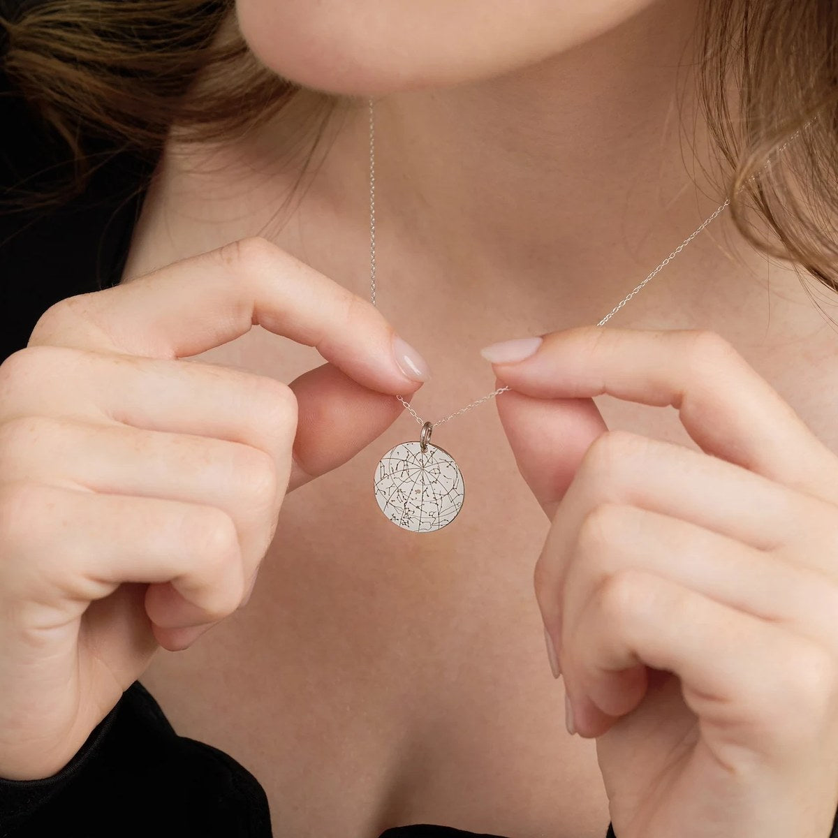 Silver star map pendant held between two fingers