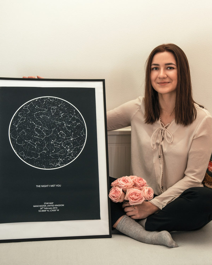 Woman sitting beside a black framed star map with roses